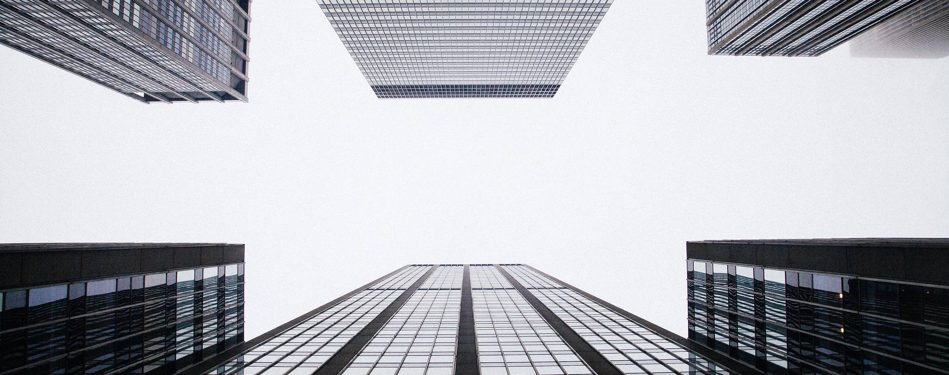 Upward view of modern glass office towers against a bright white sky