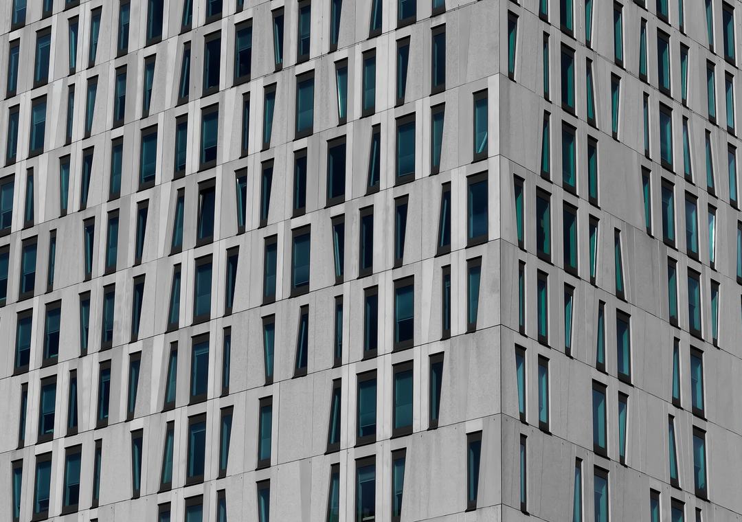 Corner of a modern grey office building with rows of narrow vertical windows